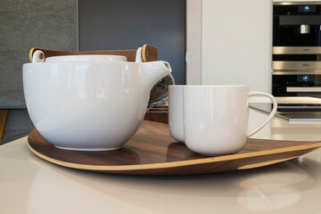 Close-up of tea utensils on a wooden tray on the kitchen table - two white cups and a ceramic teapot