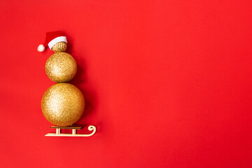 Christmas snowman made of golden Christmas balls of different sizes on a red background. Santa's red hat on a snowman, and rides on a sled. Christmas creative. Copy space.