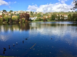 Fototapeta na wymiar Vue d'un étang en ville par temps ensoleillé, avec reflets des nuages dans l'eau