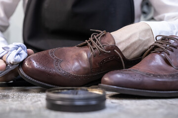 a man cleans a brown pair of shoes with a soft cloth and cream to a shine