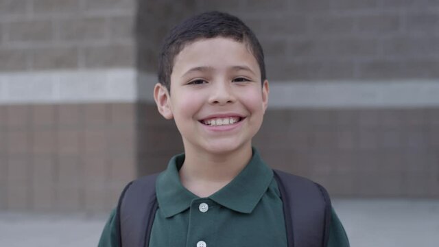 Happy young hispanic student boy smiles at camera outside a school