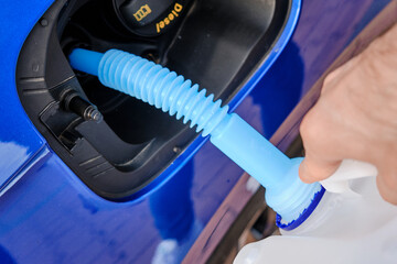 Close up filling of diesel exhaust fluid from canister into the tank of blue car for reduction of...