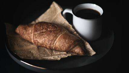 Close up view of fresh baked croissant wrapped on piece of paper with a fresh hot coffee cup simple morning breakfast