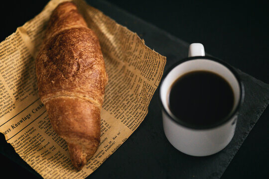 View of freshly baked croissant on a piece of newspaper with a cup of hot coffee simple morning breakfast copy space message