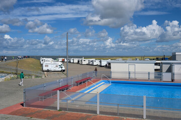 Blick über das Freibad von Harlesiel auf die Wohnmobil-Stellplätze am Hafen und Urlauber auf dem Deich an der Nordseeküste - Stockfoto