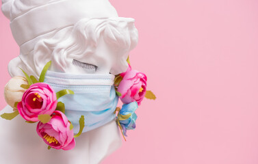 Sculpture of antique girl made of plaster in medical mask with flowers against pink background coronavirus pandemic COVID
