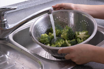 there is broccoli in a colander, it is washed under running water