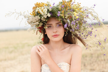 beautiful woman with a wreath on her head sitting in a field in flowers. The concept of beauty, free life and naturalness