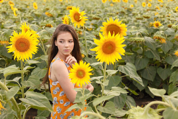 Young beautiful woman enjoying summer, youth and freedom, holding sunflowers against blue sky. Image toned.