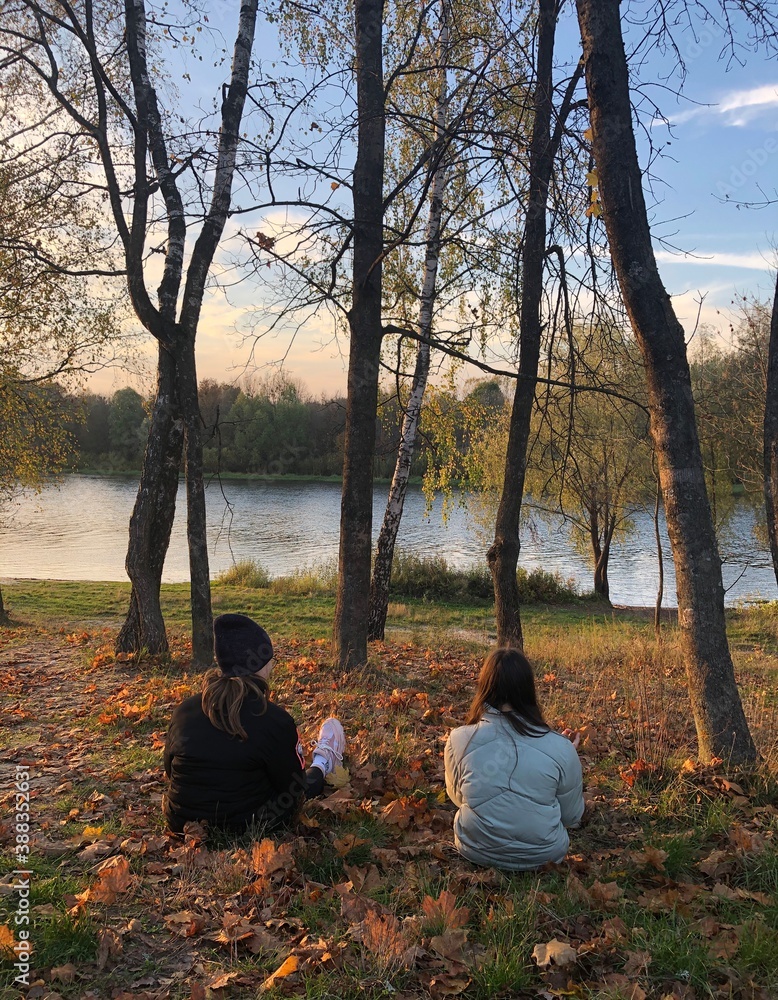 Wall mural two girls are sitting on the banks of the river on a slope in the autumn forest