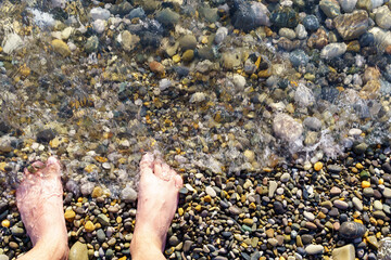 view of a man feet into the pebbles on the beach with water flowing. space for copying text