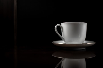 Obraz premium Noble white mug on a saucer on a dark background.