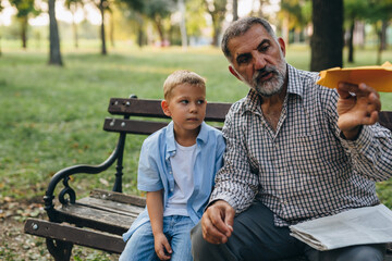 boy playing with paper plane in city park with his grandfather