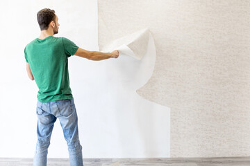young man tearing old wallpaper off the wall with copy space