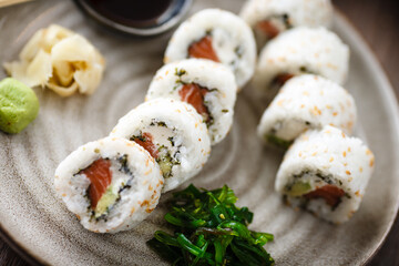 Sushi maki rolls Philadelphia with salmon, creamy cheese and avocado on a plate with chopsticks, soy sauce, wasabi and ginger. Japanese traditional seafood served for lunch in modern restaurant
