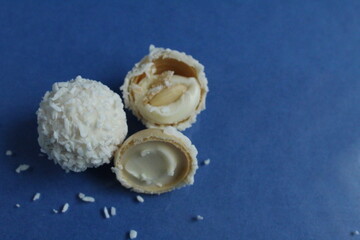 three white with coconut candies and half with a waffle and white cream like Raffaello on a blue bright background with copy space for text