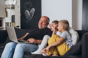 father sitting sofa with his children and using laptop computer at home