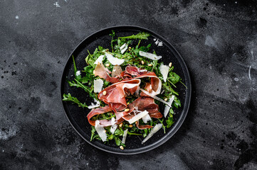 Salad with Parma, prosciutto ham, arugula and Parmesan. Black background, top view, space for text