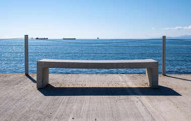 Empty bench on concrete deck, sea view, blue sky background.