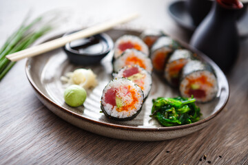 Sushi maki rolls with tuna, flying fish caviar, crab, avocado on a plate with chopsticks, soy sauce, wasabi and ginger. Japanese traditional food closeup served for lunch in modern gourmet restaurant