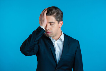 Frustrated european business man in suit over blue wall background. Guy is tired, bored of work or...