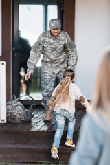 Little girl running to military man standing on house threshold with blurred woman on foreground