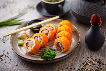 Sushi maki rolls California Futomaki with salmon, avocado, cucumber, crab and flying fish roe on a plate with chopsticks, soy sauce, wasabi and ginger. Japanese traditional seafood served restaurant