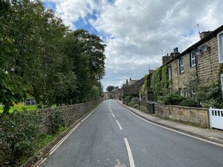 Looking down, Main Street, in the village of Eastby, with trees, stone cottages, and a cloudy sky 