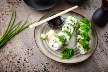 Sushi maki rolls with cucumber, avocado, tomato, creamy cheese, chuka wakame on a plate with chopsticks, soy sauce, wasabi and ginger. Japanese traditional seafood served for lunch in restaurant