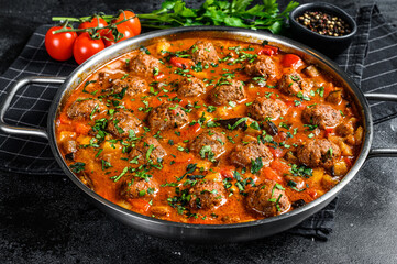Pork meatballs with tomato sauce and vegetables in a pan. Black background. Top view