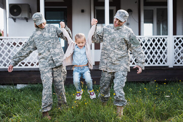 Happy military mother and father lifting daughter over grass on backyard near house
