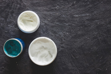 Top view of blue and white creams in jar. Hand creams and gel on dark grey background with copy space.