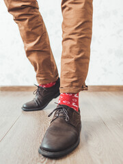 Young man pulls up leg of his chinos trousers to show bright red socks with reindeers on them. Scandinavian pattern. Winter holiday spirit. Casual outfit for New Year and Christmas celebration.