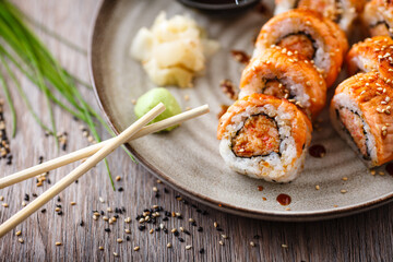 Baked sushi maki rolls with salmon, crab and spicy sauce on a plate with chopsticks, soy sauce, wasabi and ginger. Japanese traditional fish food closeup served for lunch in modern gourmet restaurant