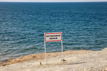 Sign "Caution cliff" at the edge of the cliff in the sea
