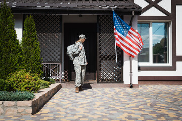Military servicewoman with backpack leaving house, standing on threshold
