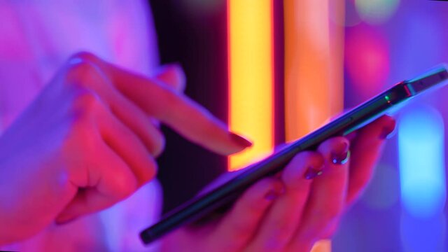 Woman using smartphone device at interactive exhibition or museum with purple illumination - scrolling and touching - close up side view. Futuristic, retrowave, immersive, entertainment concept