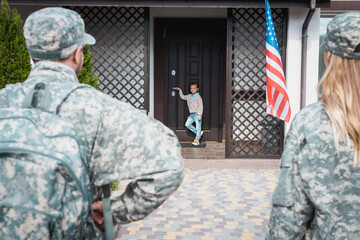 Girl standing on threshold with blurred military couple on foreground