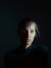 Studio portrait of young pretty girl with shadows on face on black background