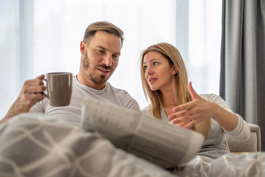 Young couple sitting in bed in the morning, reading newspapers and drinking coffee together