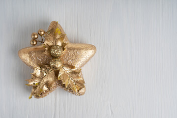 Top view of single Christmas or New Year decoration in shape of golden star with hollen or English holly leaves on white wooden background. Image with copy space, horizontal orientation