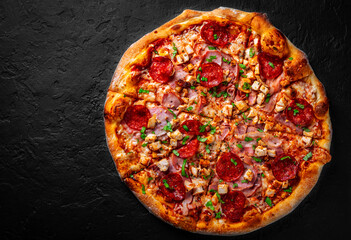 Pizza with Mozzarella cheese, salami, chicken meat, bacon, ham, Tomato sauce, pepper, spices. Italian pizza on Dark grey black slate background