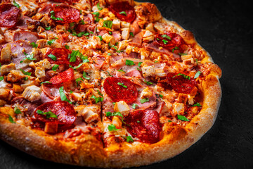 Pizza with Mozzarella cheese, salami, chicken meat, bacon, ham, Tomato sauce, pepper, spices. Italian pizza on Dark grey black slate background