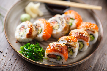 Sushi maki rolls with salmon, eel, avocado, cucumber on a plate with chopsticks, soy sauce, wasabi and ginger. Japanese traditional fish food closeup served for lunch in modern gourmet restaurant