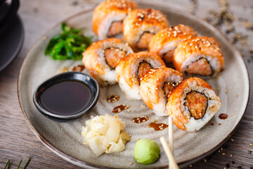 Baked sushi maki rolls with salmon, crab and spicy sauce on a plate with chopsticks, soy sauce, wasabi and ginger. Japanese traditional fish food closeup served for lunch in modern gourmet restaurant