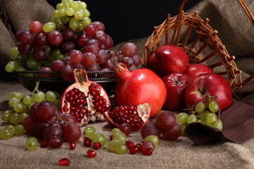 Vase with grapes, pomegranates and apples on a background of burlap