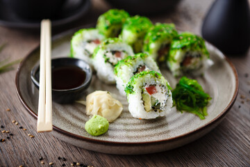Sushi maki rolls with cucumber, avocado, tomato, creamy cheese, chuka wakame on a plate with chopsticks, soy sauce, wasabi and ginger. Japanese traditional seafood served for lunch in restaurant