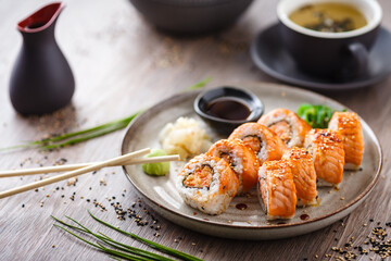Baked sushi maki rolls with salmon, crab and spicy sauce on a plate with chopsticks, soy sauce, wasabi and ginger. Japanese traditional fish food closeup served for lunch in modern gourmet restaurant