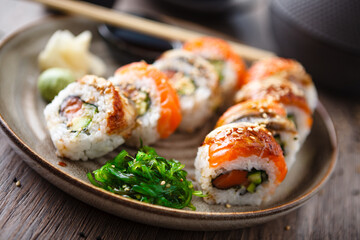 Sushi maki rolls with salmon, eel, avocado, cucumber on a plate with chopsticks, soy sauce, wasabi and ginger. Japanese traditional fish food closeup served for lunch in modern gourmet restaurant