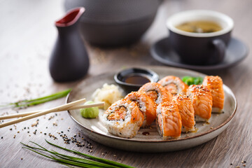 Baked sushi maki rolls with salmon, crab and spicy sauce on a plate with chopsticks, soy sauce, wasabi and ginger. Japanese traditional fish food closeup served for lunch in modern gourmet restaurant